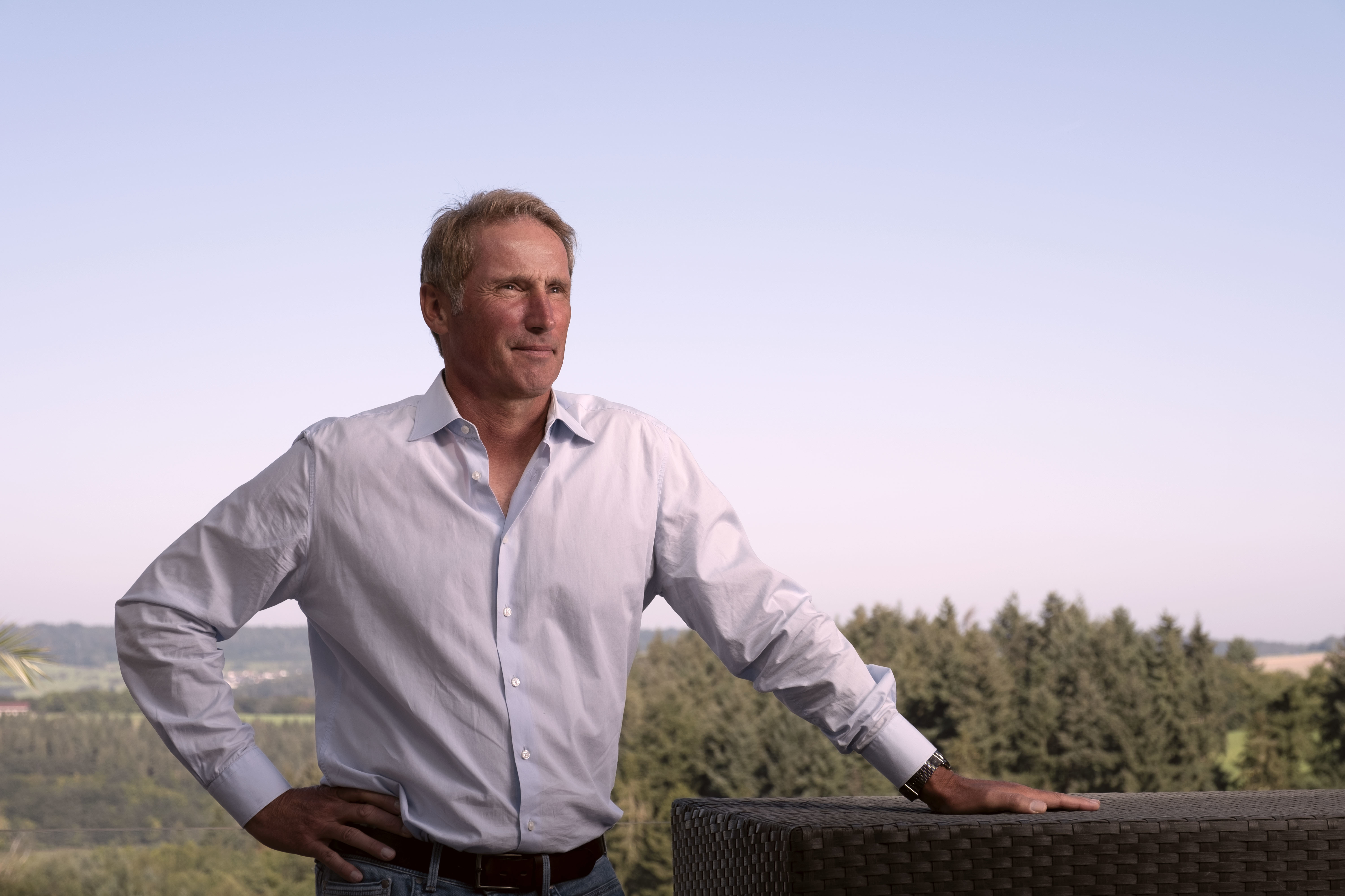 Stefan Burchard, Life-Performance-Coach und Leiter der Mentalen Tennis Akademie, steht im Freien vor einer natürlichen Landschaft, trägt ein leichtes Hemd und Jeans und zeigt eine selbstsichere Haltung.