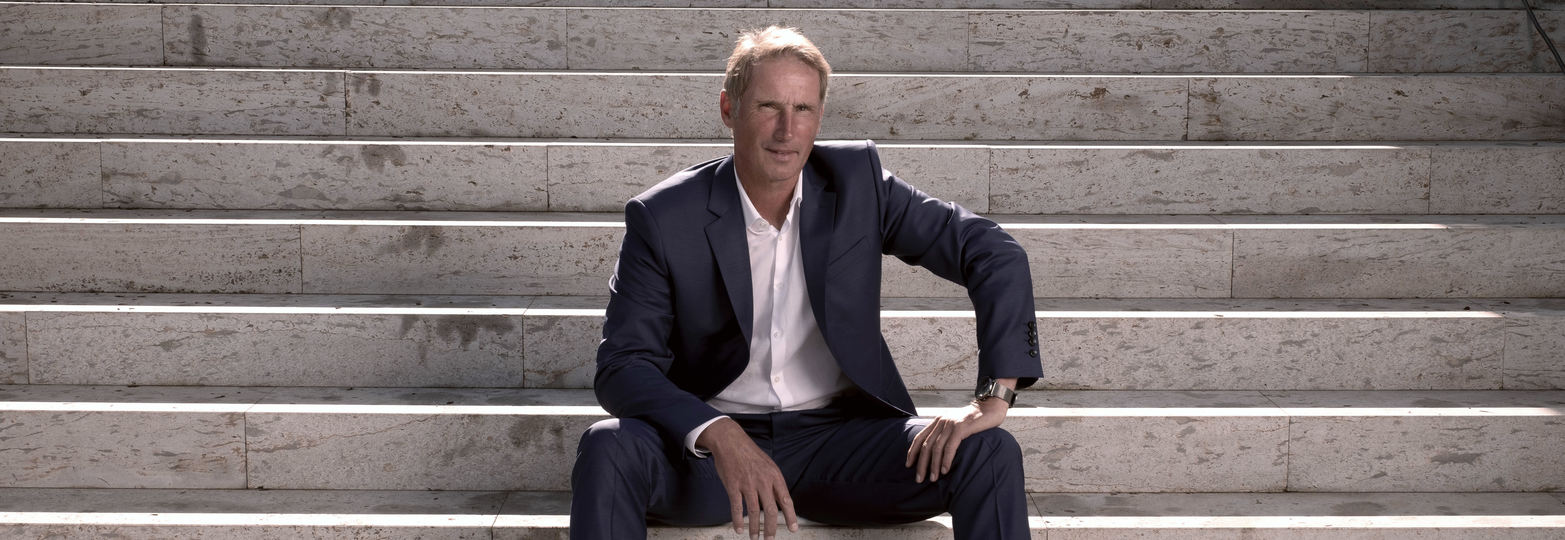 Stefan Burchard, Life-Performance-Coach, Speaker und ehemaliger Tennis-Weltmeister, sitzt auf steinernen Stufen in einem dunklen Anzug – er verbindet Spitzensport-Erfahrung mit mentaler Stärke-Methoden für Coaching, Impulsvorträge und Seminare.