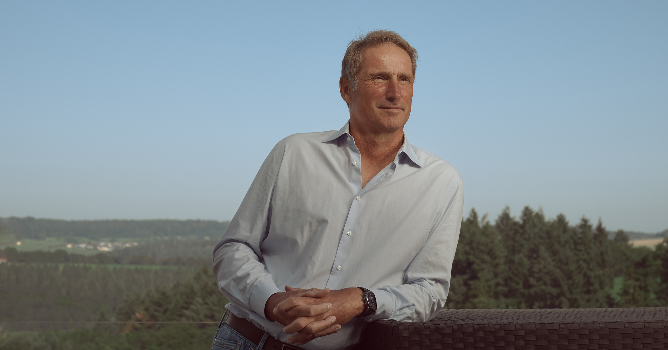 Stefan Burchard, Life-Performance-Coach und ehemaliger Tennis-Weltmeister, steht im Freien vor einer landschaftlichen Kulisse, lehnt an einem Geländer.