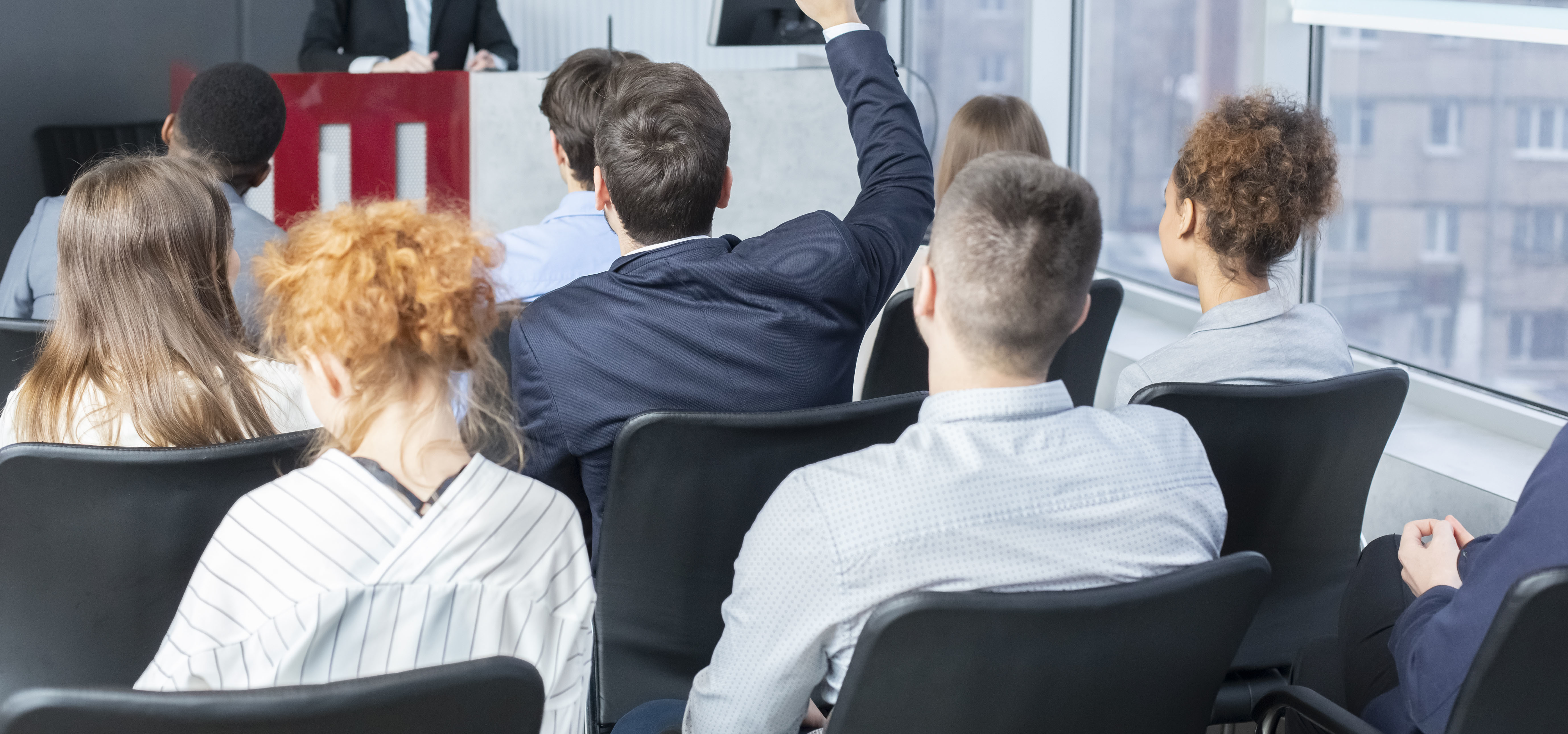 Ein Auditorium bei einem Vortrag oder Seminar, bei dem ein Teilnehmer die Hand hebt, um sich zu beteiligen—passend zu Angeboten für mentale Stärke und persönliche Leistungsfähigkeit.